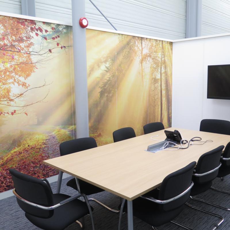 View of large meeting table, TV screen and back wall with photograph of autumn coloured tree scene and rays of sun shining through