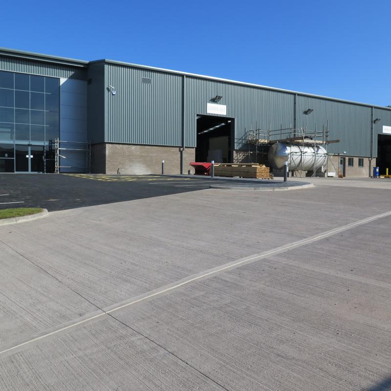 external view of new large grey metal clad building with large concrete carpark in front of two tall roller shutter doors